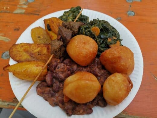 Gemischter Teller aus Kamerun: Bohnen, Spinat, Fleischspieß, Krapfen und Kochbananen
