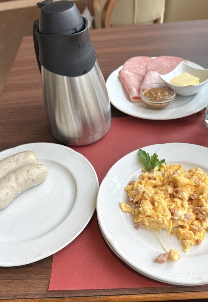 Serviertes Frühstück nach Wahl: Weißwürste, Rührei mit Speck und Käse, dazu Schinken und Salami für die Semmel