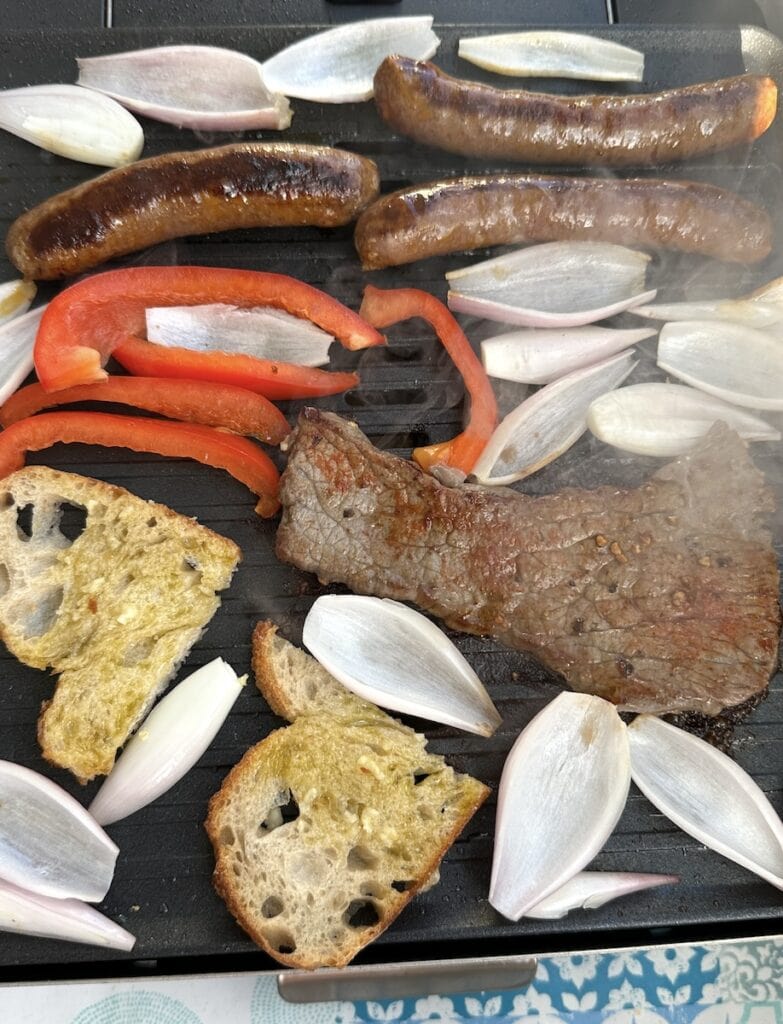 Grill mit Minutensteaks, Knoblauchbrot, Merguezwürsten, Paprika und Zwiebeln