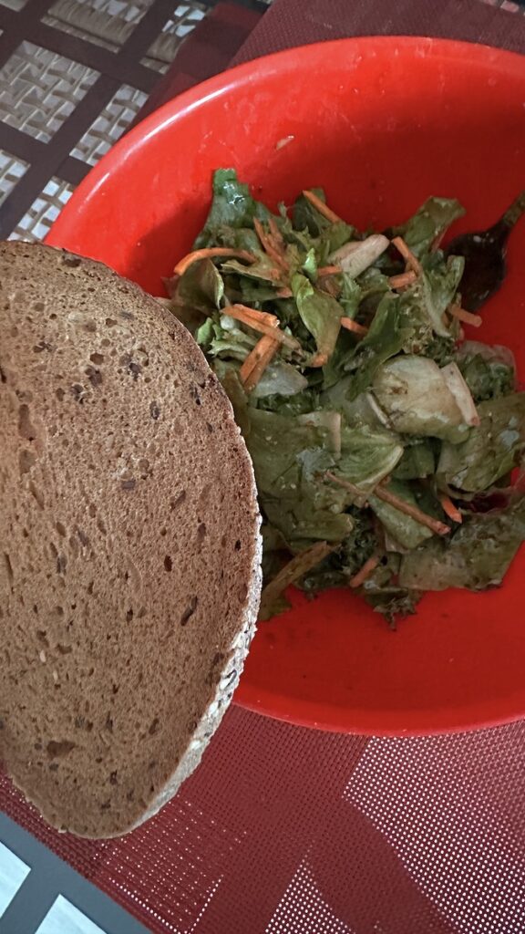 Salat in einer roten Schüssel und eine Scheibe Brot auf der Schüsselkante liegend