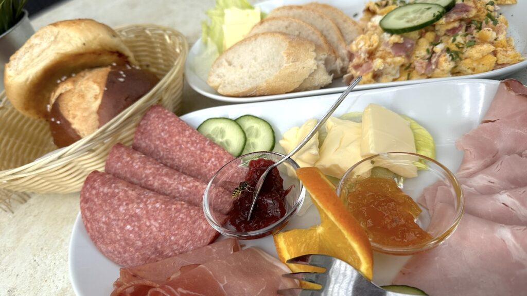 Frühstück (Brötchen, Schinken, Salami, Marmelade) mit Rühreiern mit Salami, Schinken und Speck