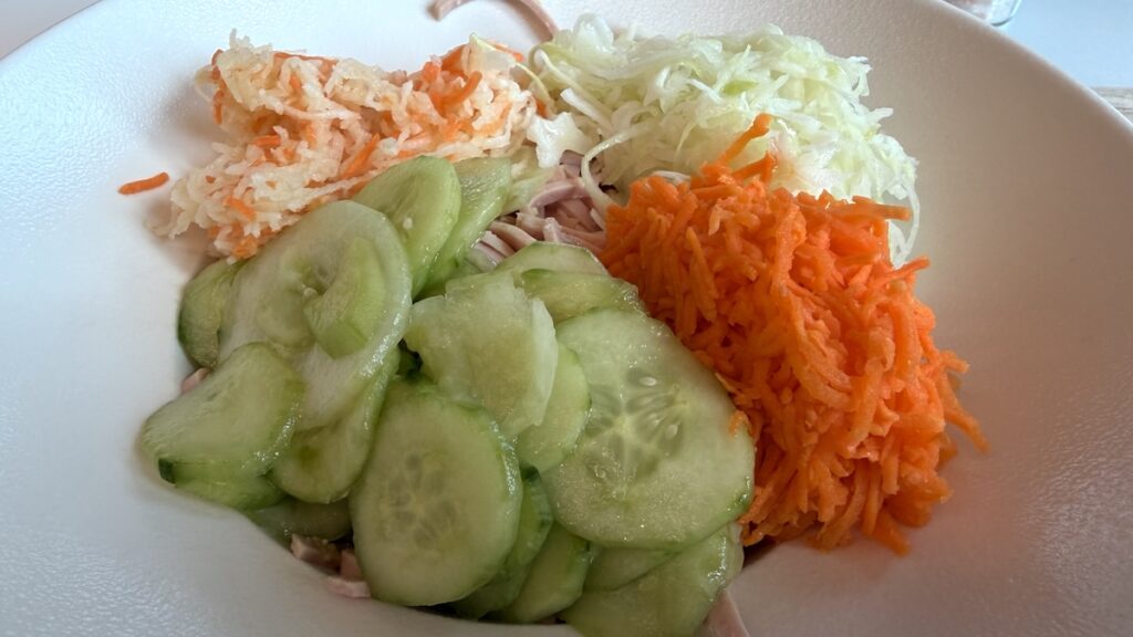 Ein großer Teller Wurstsalat, versteckt unter Gurken- Kraut- und Karottensalat